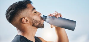 Man drinking from a water bottle thinking about the Role of Hydration in Chafing and Sweat Rash Prevention