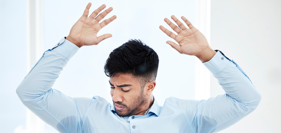 A man lifting his arms and looking at his underarm sweat being concerned