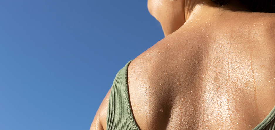 Woman in a green vest top, with a sweaty back on a blue background. 7 reasons your might be sweating too much.