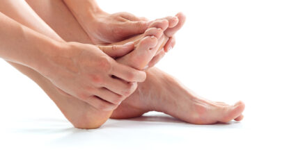 Why do we get fungal nail infections? A person with bare feet is holding on to their foot with both hands