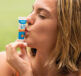 A woman kissing a tube of Dermal Therapy SPF 50 Lip Balm on a green background.