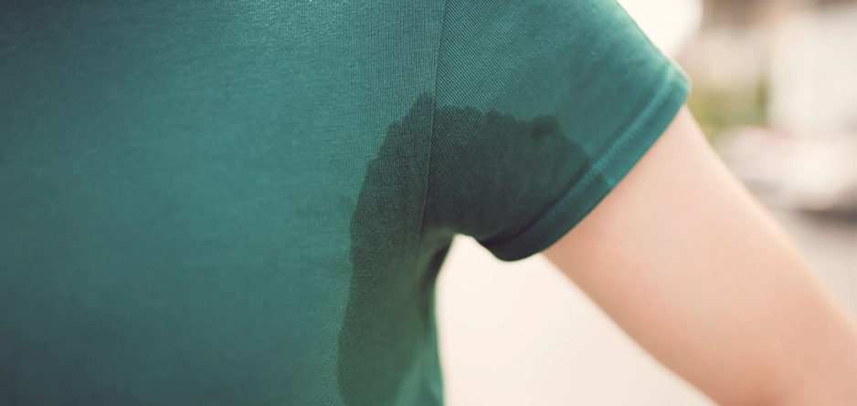 closed up image of models underarm where a dark green top shows a sweat mark