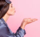 A woman in purple silk PJs blowing a kiss on a pink background - Do lip sleeping masks work?