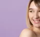 A girl with some acne on her face smiling on a purple background