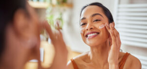 Young smiling woman applying a skin care product on her face