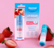 Dermal Therapy Lip Balm Strawberry packaging and lip balm displayed with whole and sliced strawberries on a pink background