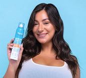 Liv Rahmé holding a Dermal Therapy Dry Shampoo on a blue background