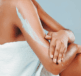 A person with a white towel wrapped around them rubbing a skin cream containing Urea on to the dry skin on their arm.