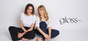 Sarah Tarca and Sherine Youssef seated on the floor against a white background, wearing casual outfits—one in a white t-shirt and dark pants, the other in a white shirt and jeans—with the Gloss Etc logo positioned to the right.