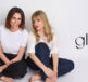 Sarah Tarca and Sherine Youssef seated on the floor against a white background, wearing casual outfits—one in a white t-shirt and dark pants, the other in a white shirt and jeans—with the Gloss Etc logo positioned to the right.