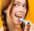 Person holding Dermal Therapy Lip Balm SPF50+ Stick near their mouth against an orange background.