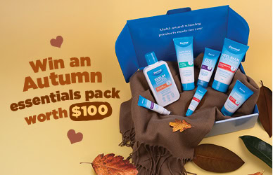 Landscape promotional image showing a blue open gift box filled with Dermal Therapy skincare products on a brown cloth, surrounded by autumn leaves, with text that reads ‘Win an Autumn essentials pack worth $100.