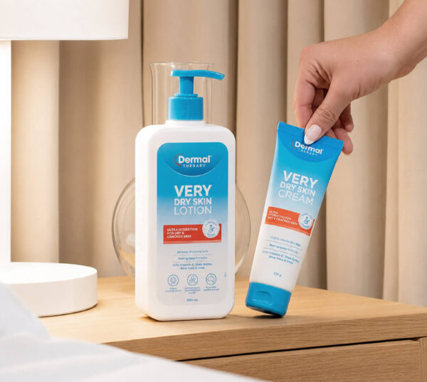Dermal Therapy Very Dry Skin Lotion bottle and Very Dry Skin Cream tube displayed on a wooden stand, with a hand holding the cream tube