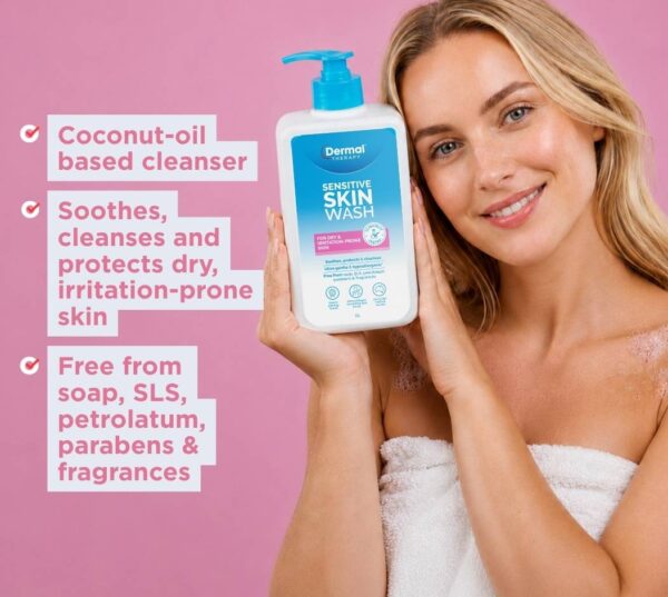 Person holding a bottle of Dermal Therapy Sensitive Skin Wash against a pink background with visible product feature text.
